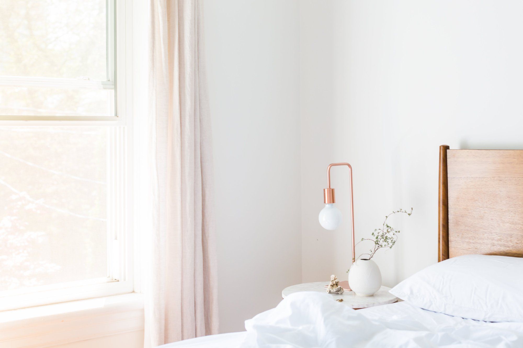 El rincón de un dormitorio: cama deshecha, lámpara de cobre y cortina rosa